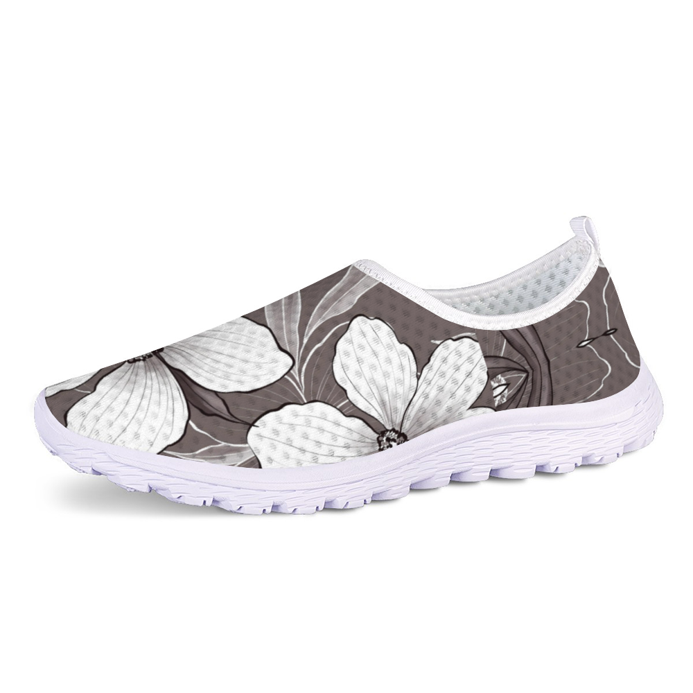 Introducing the White Blossoms Kushion Kicks, a chic slip-on shoe showcasing a black and white floral design on the upper, paired with a slip-resistant textured white sole.