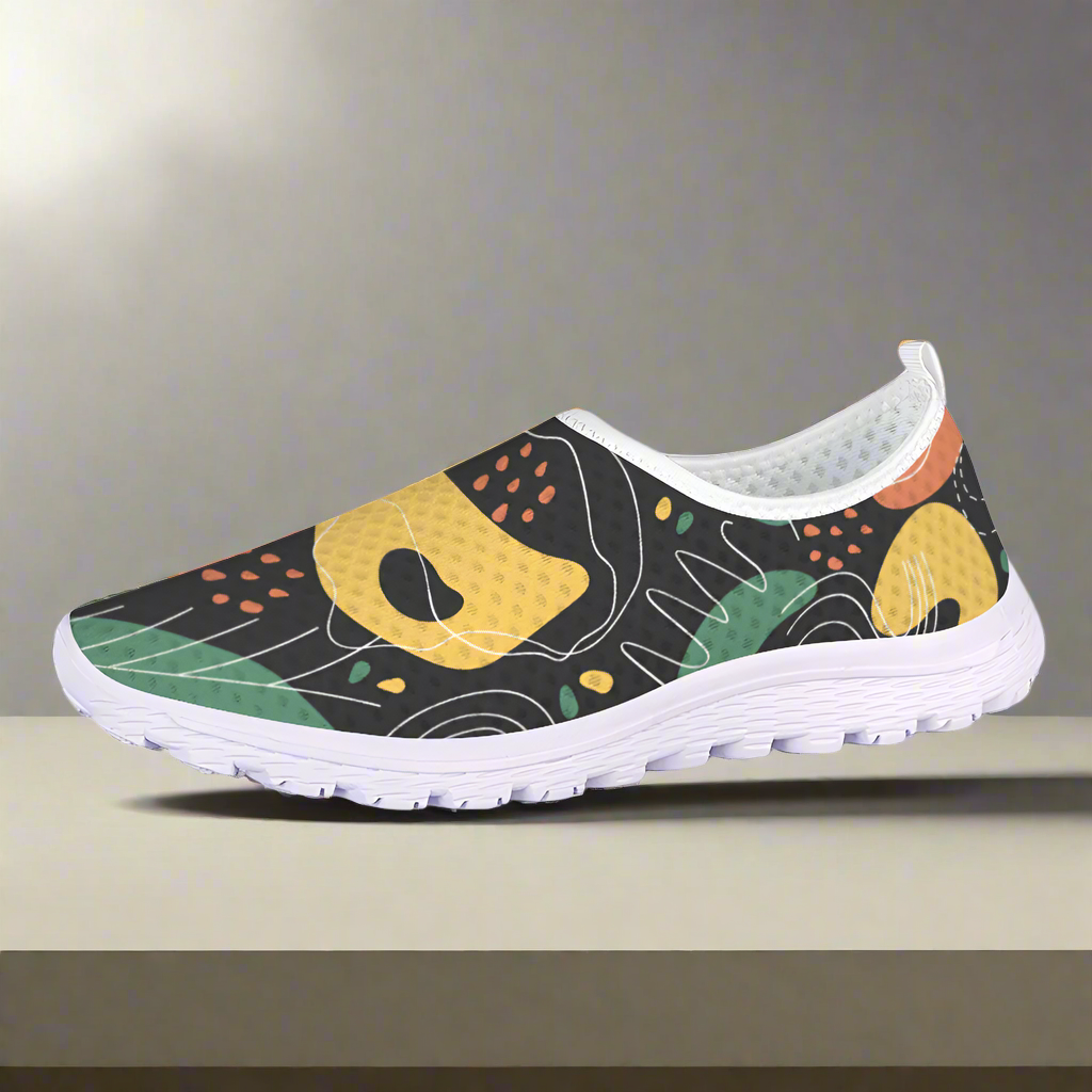 Introducing the Autumn Maze Cushion Kicks, a lightweight slip-on athletic shoe designed with a white sole and a breathable black upper mesh fabric featuring abstract multicolored patterns in green, yellow, orange, and white. Perfect for walking and everyday comfort.